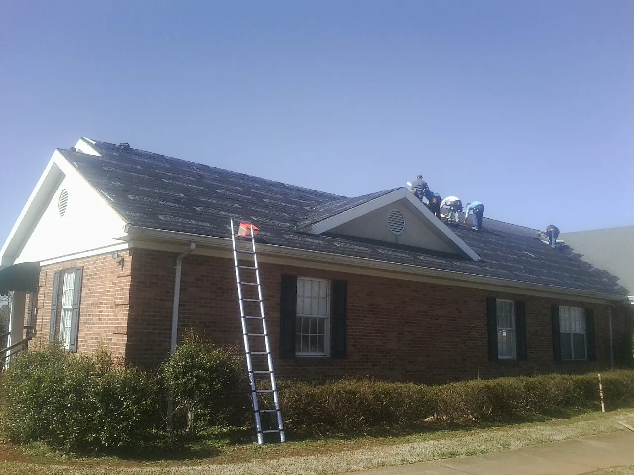 Crew tearing shingles off a brick ranch roof with a ladder set — Metal Roof Repair work by our crew in Poughquag