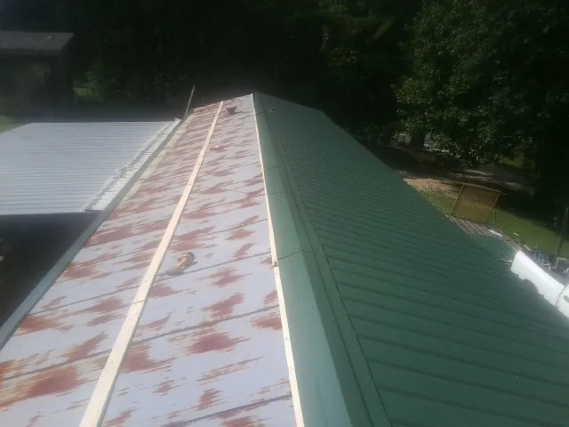 Old rusted panels beside newly installed green metal roofing — Wind Damage Roof Repair by Roofing Brothers in Poughquag