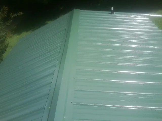 New green metal panels meeting at the ridge of a roof — Flat Roof Repair work by our crew in Poughquag