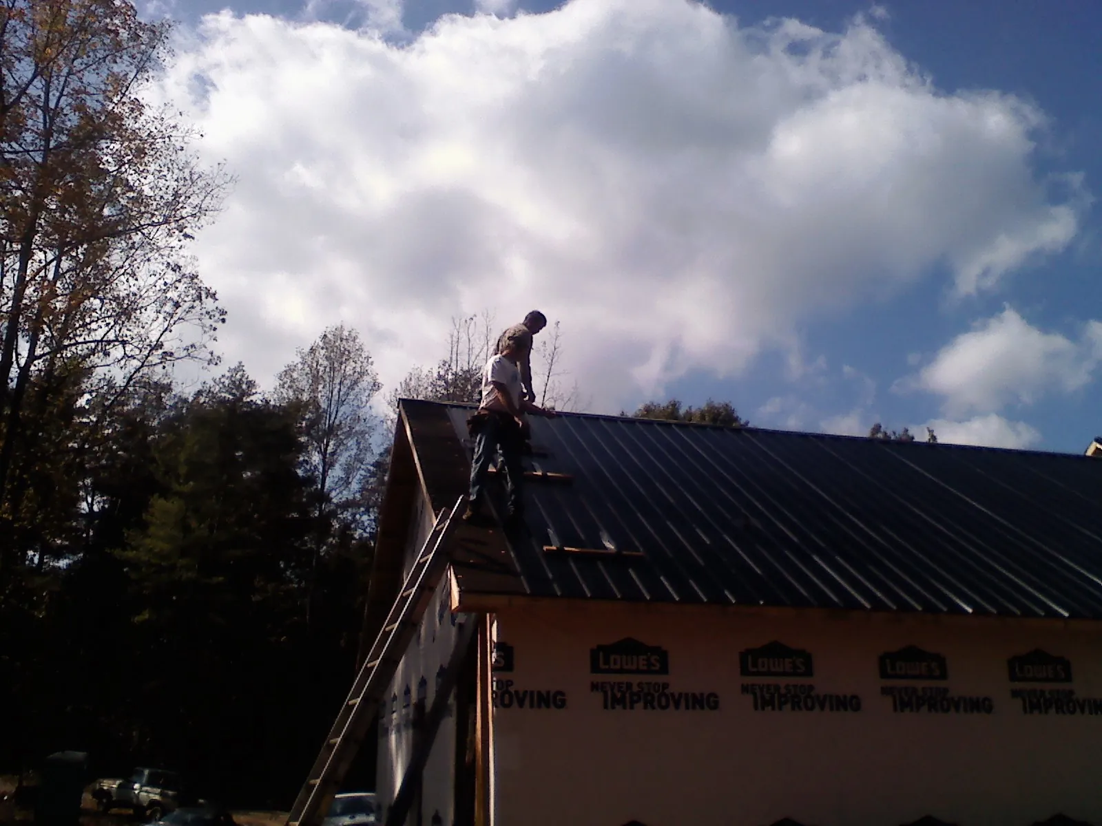 Roofer fastening dark metal panels high against a cloudy sky, from a Roof Inspection job in Poughquag