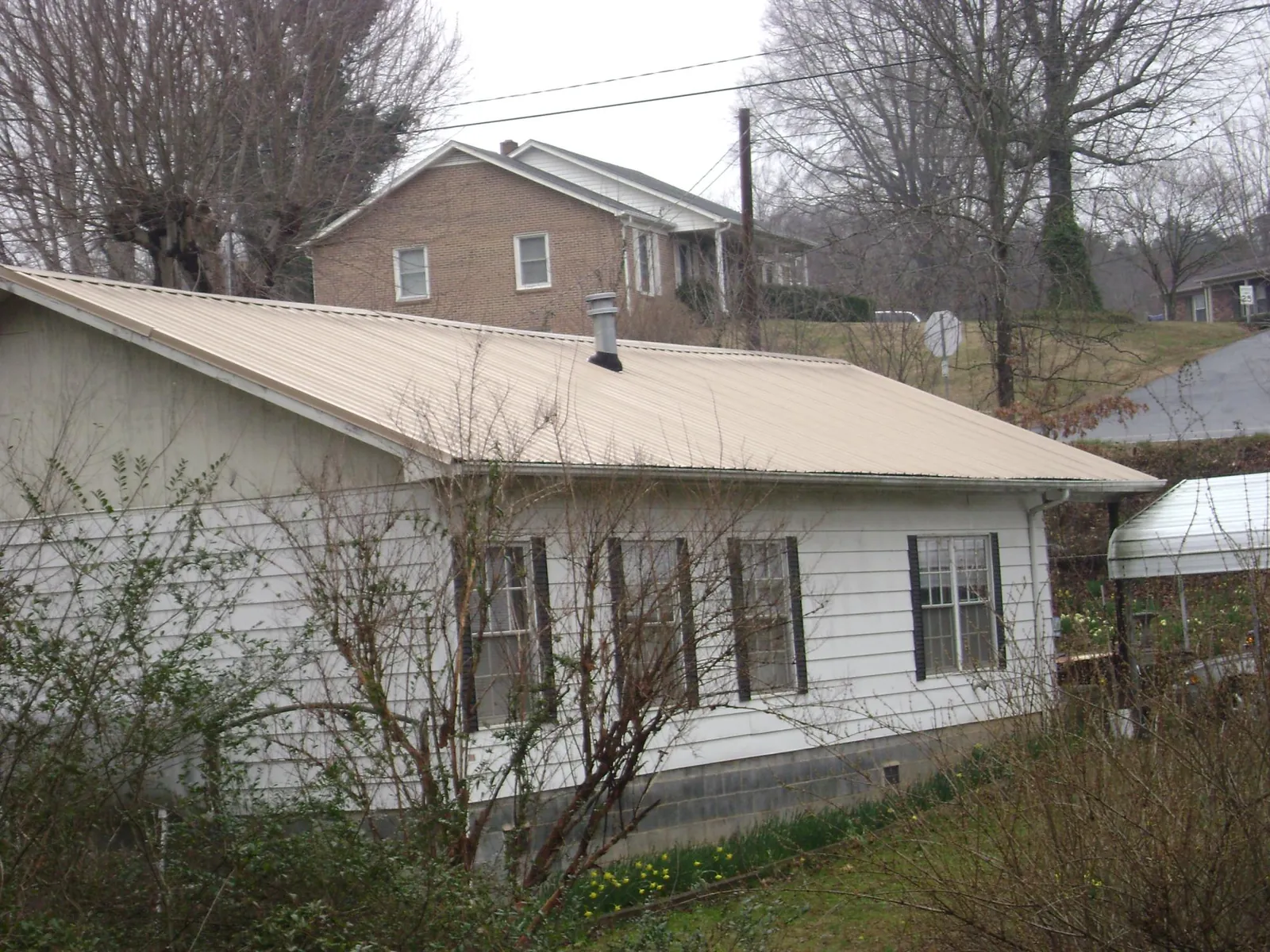 Tan metal roof on a white sided house set into a hillside — Commercial Roofing by Roofing Brothers in Poughquag